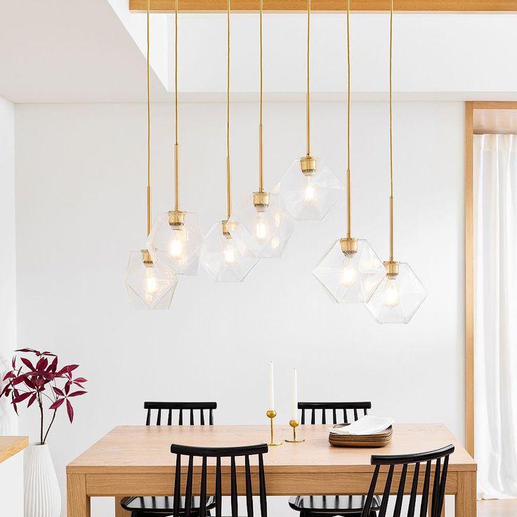 a dining room table with black chairs and lights hanging from the ceiling