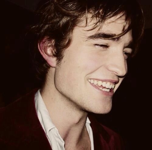 a young man smiling while wearing a red vest and white shirt with his eyes closed