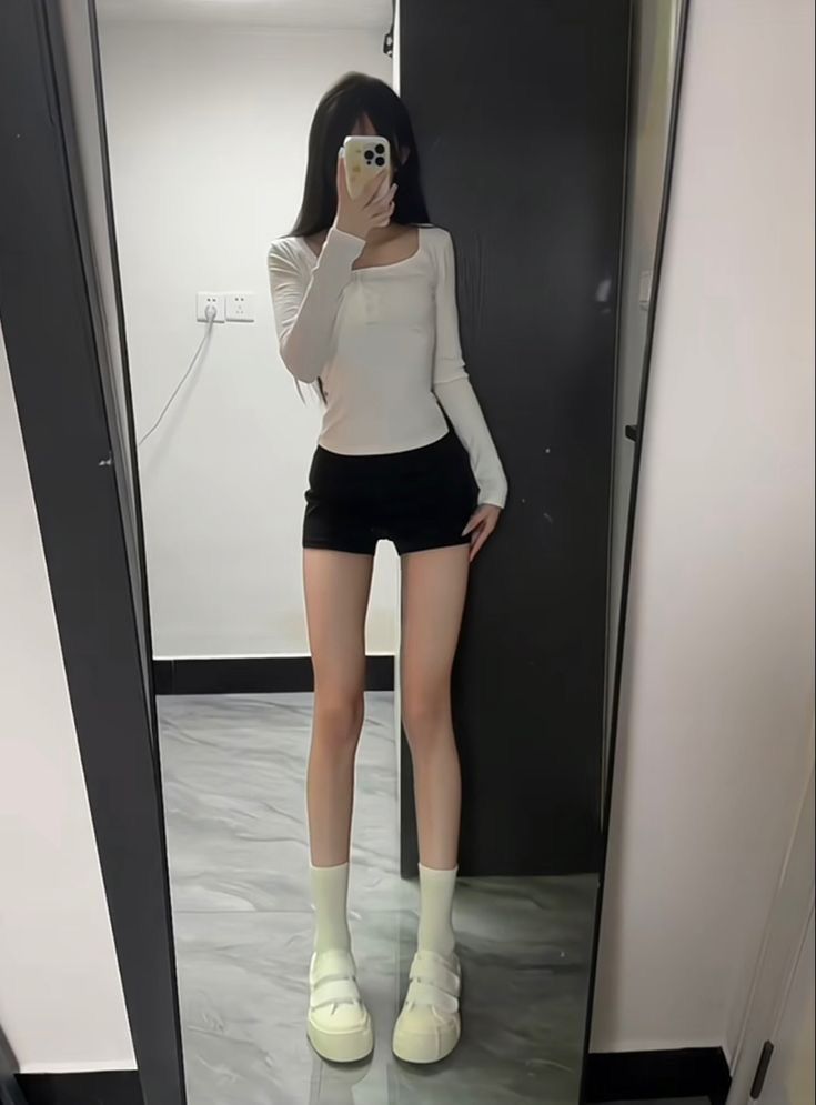 a woman taking a selfie in front of a mirror wearing short black shorts and white socks