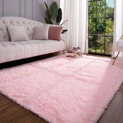 a living room with a white couch and pink rug on the wooden floor next to a window