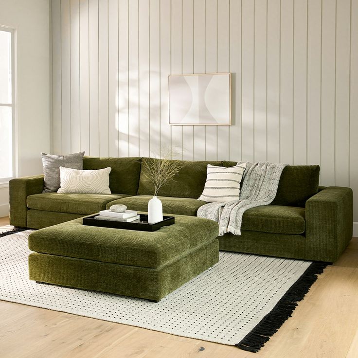 a green couch and ottoman in a living room with white walls, rugs and wood flooring