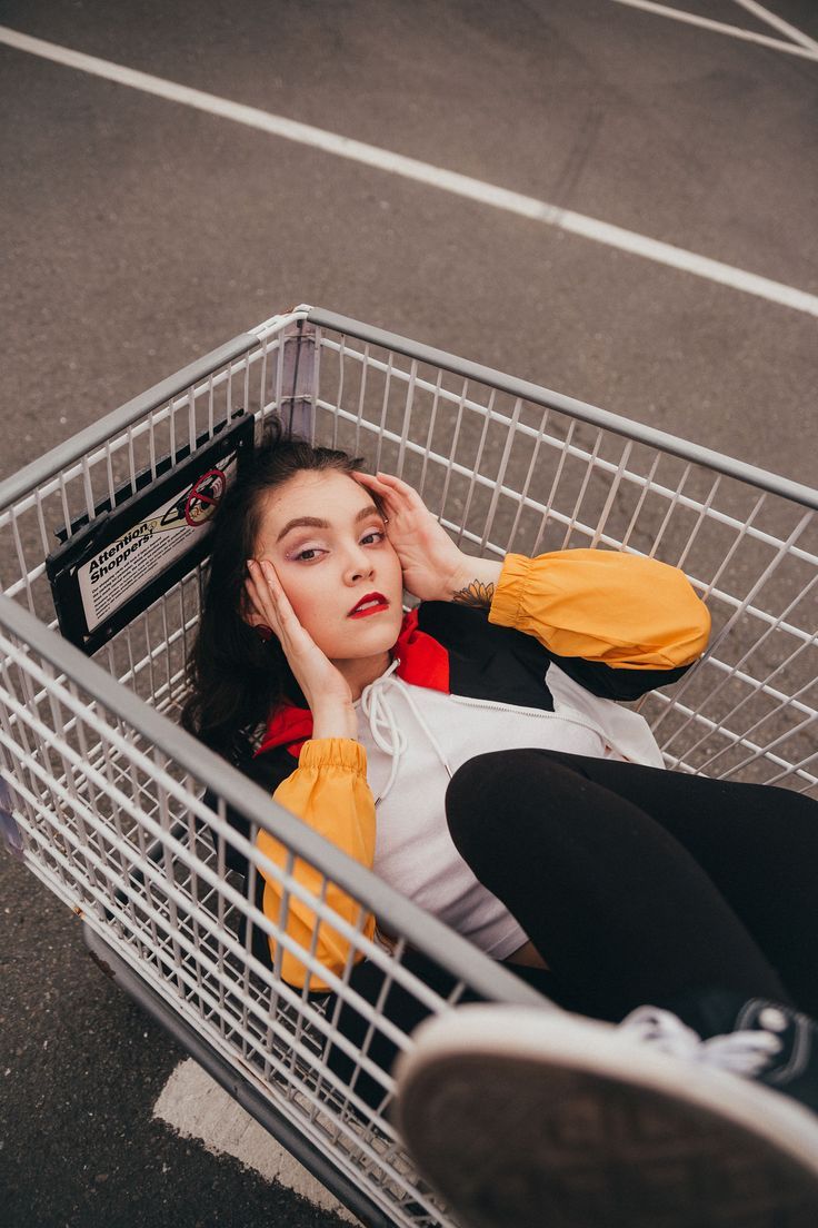 Model is laying in a shopping cart with one leg up, shoe slightly in frame and out of focus. Photographer is shooting from above. Shopping Cart Portrait, Perspective Poses Photography, 80s Poses, Street Photoshoot Poses Women, Mood Board Photoshoot, Public Photoshoot, Shopping Cart Photoshoot, Photoshoot Ideas Female, Carpark Photoshoot