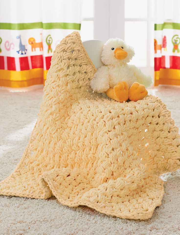 a crocheted blanket on the floor with a stuffed duck sitting on top of it