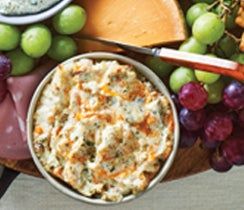 a platter with grapes, cheese and crackers next to other food on a table