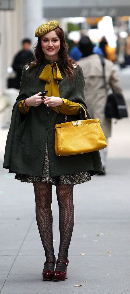 a woman walking down the street with a yellow purse on her shoulder and black tights