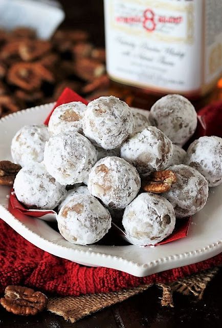 a white plate topped with powdered donuts next to a bottle of maple syrup