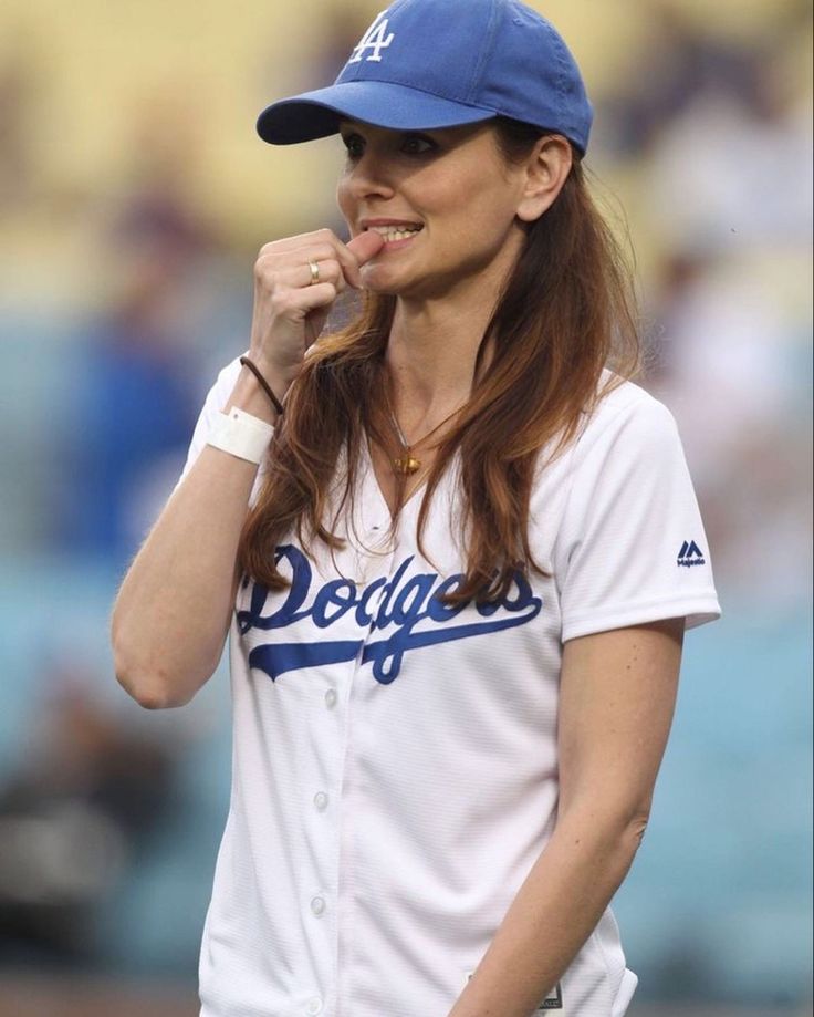 a woman in a dodgers baseball uniform is holding her finger to her mouth while standing on the field