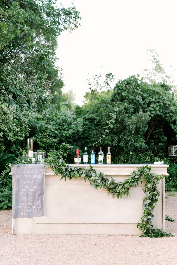 an outdoor bar with bottles and greenery on the top, next to a sign