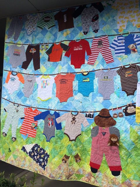 a quilted wall hanging with baby clothes on it