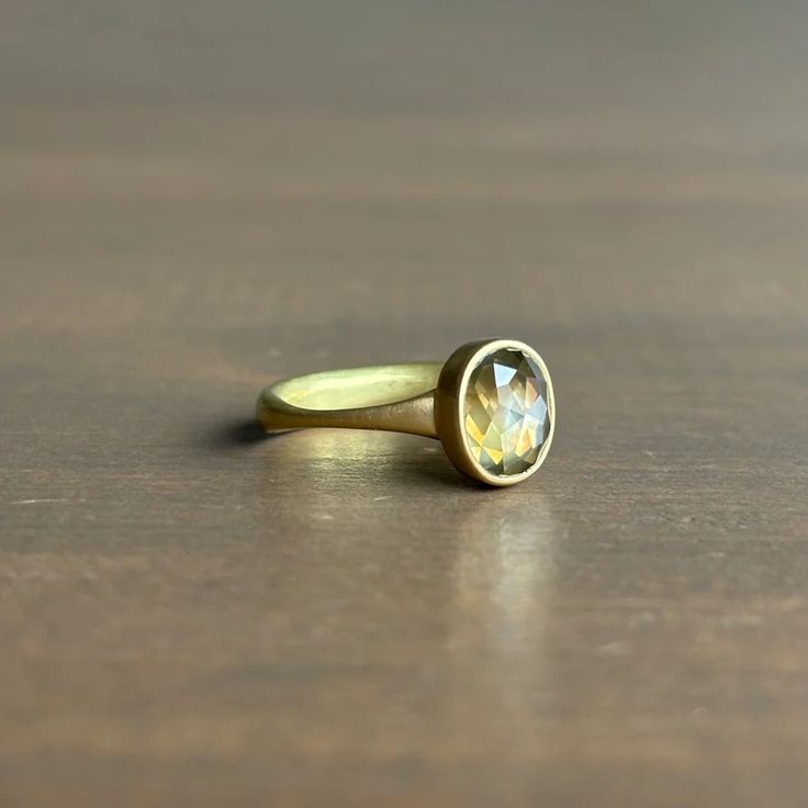 a yellow gold ring with an oval cut diamond in the center on a wooden surface