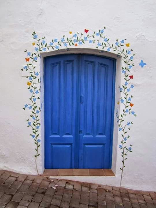 a blue door is painted on the side of a white building with flowers and vines