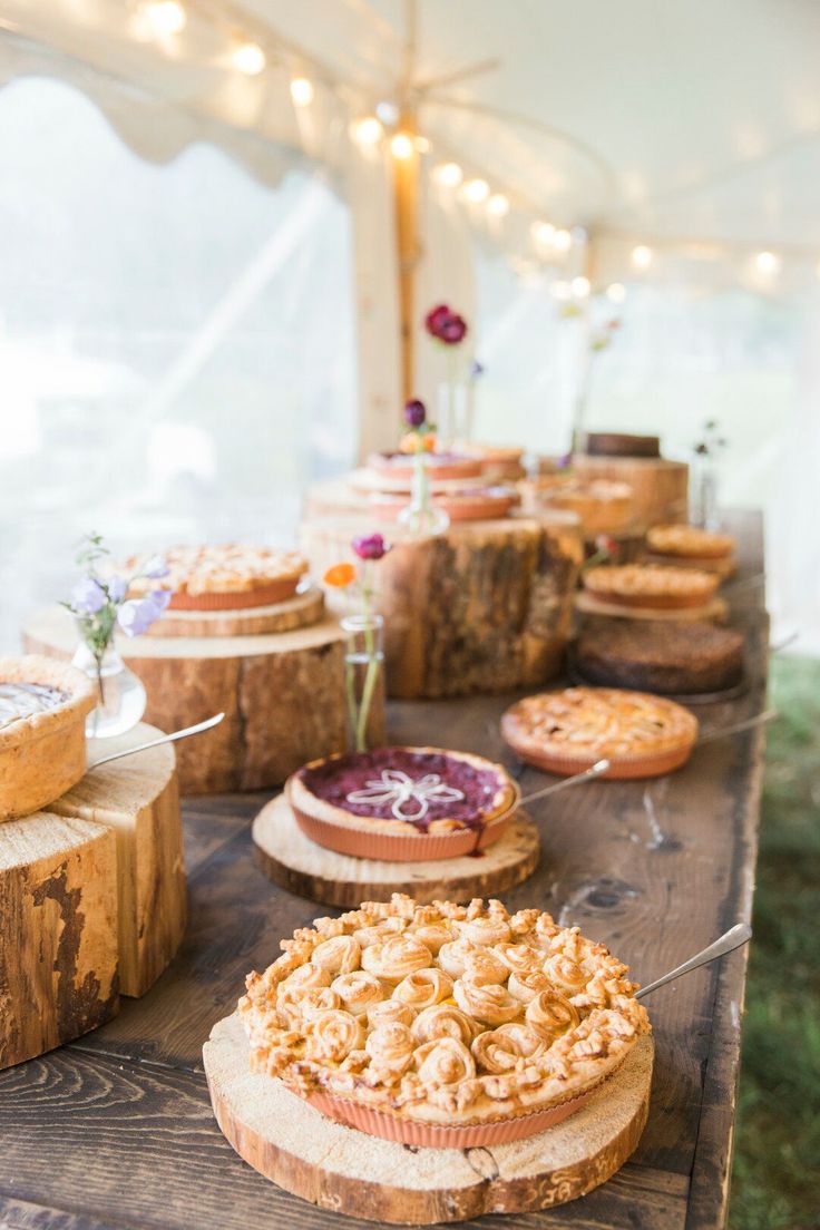 an assortment of desserts are displayed on the table at this outdoor wedding reception, which is decorated with wood slices and string lights