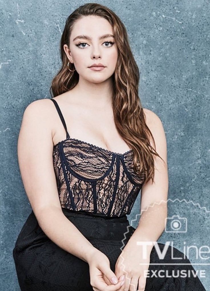 a woman sitting on top of a chair wearing a black dress and holding her hands in her pockets