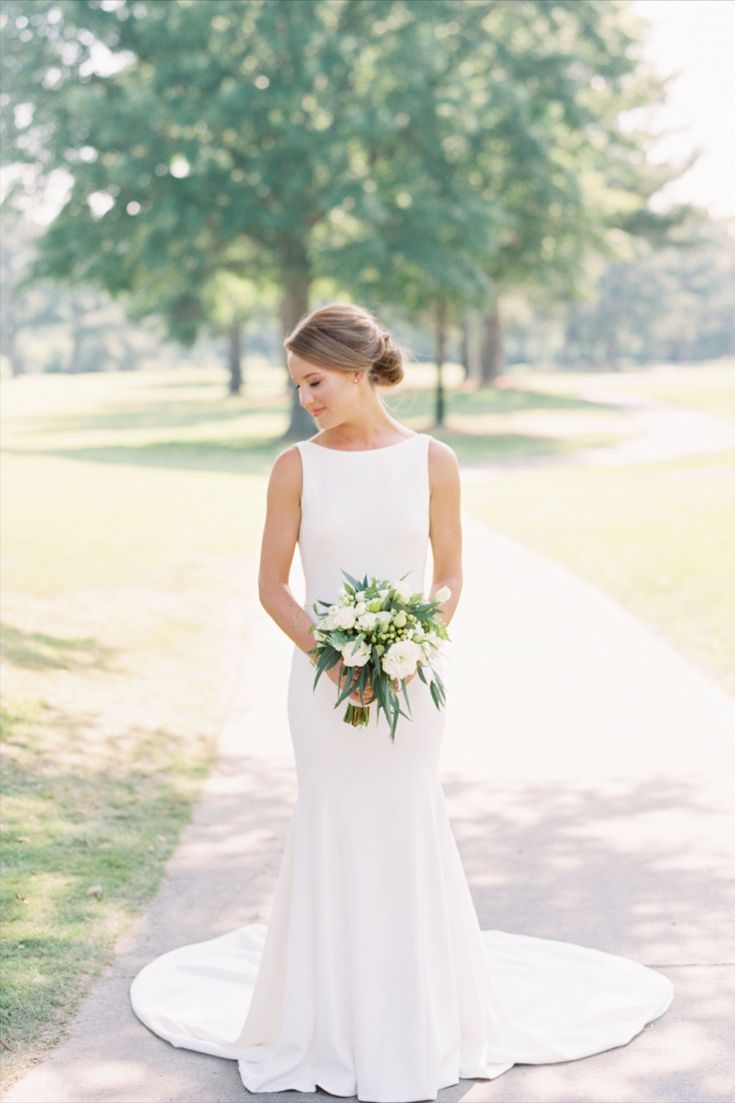 a woman in a white dress standing on a path with trees and grass behind her