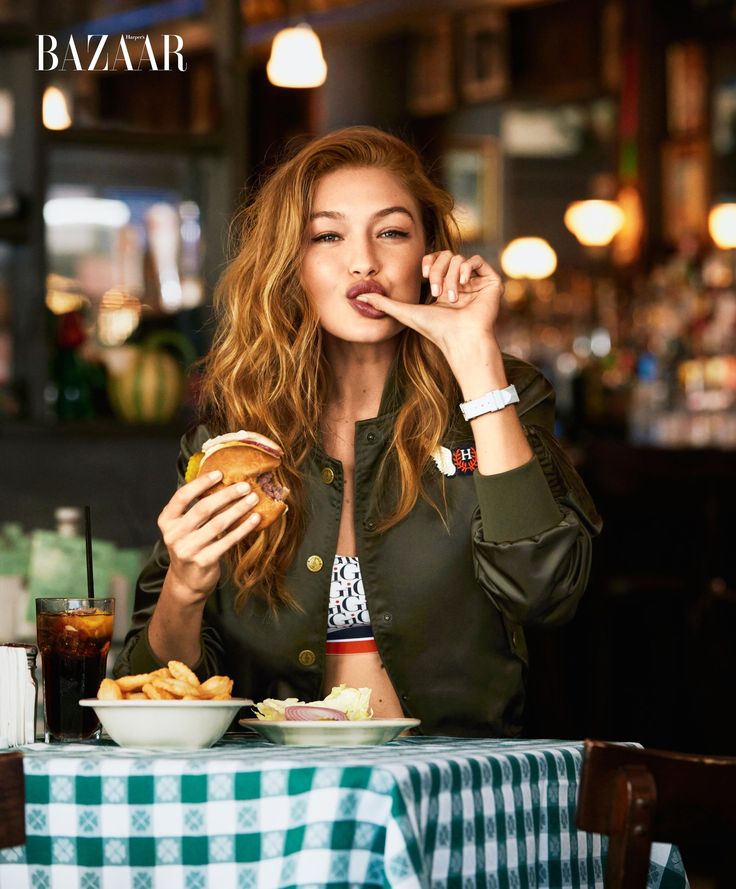 a woman sitting at a table eating food and talking on the phone while holding a hamburger in her hand