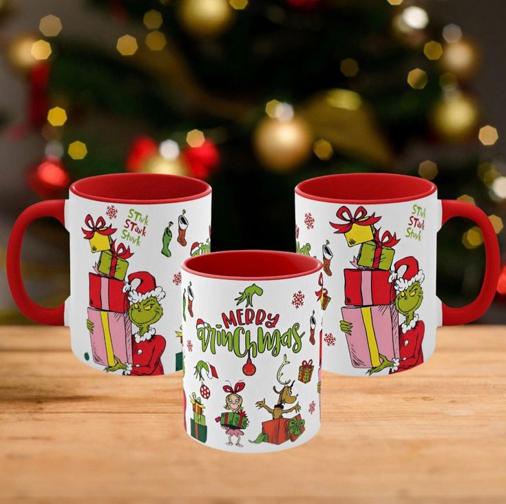 two red and white coffee mugs sitting on top of a wooden table next to a christmas tree