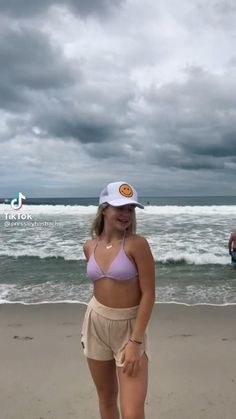 a woman standing on top of a sandy beach next to the ocean under a cloudy sky