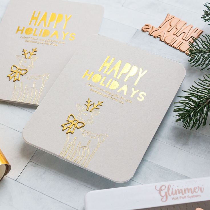 two holiday cards with gold foil on them next to a christmas tree and other decorations