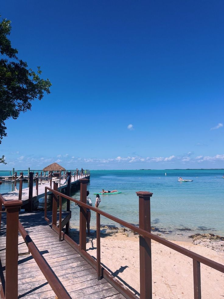 a wooden walkway leading to the beach with boats in the water and people walking on it