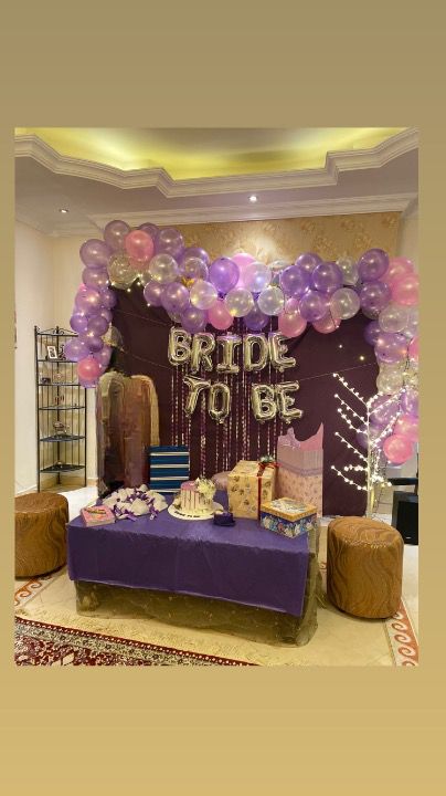 a purple and gold birthday party with balloons on the wall, cake table and chairs