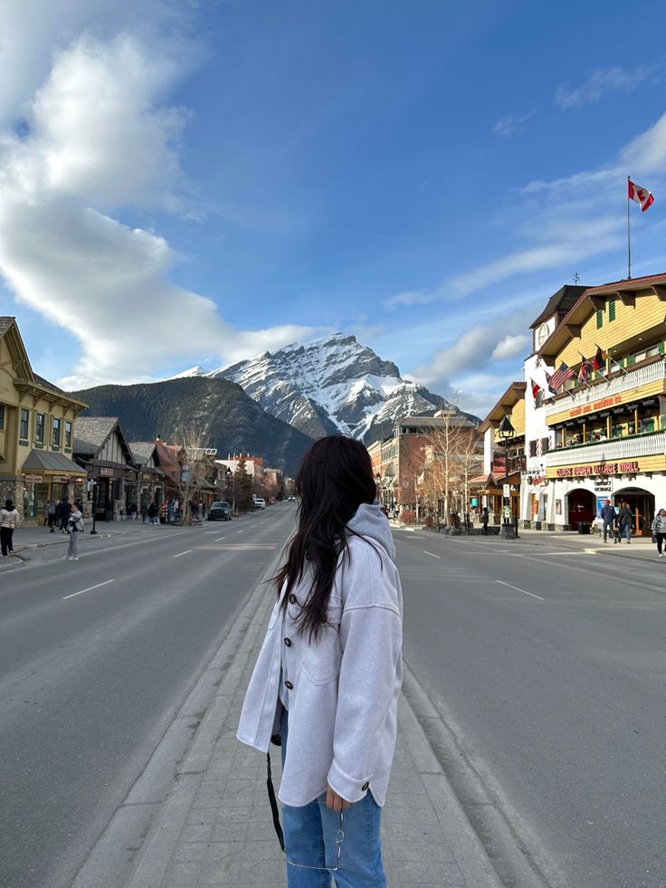 a woman standing in the middle of an empty street with mountains in the back ground