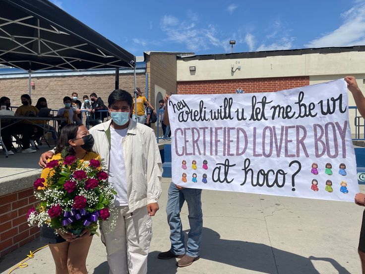 two people holding a sign that says certified lover boy at hoo? with flowers in front of them