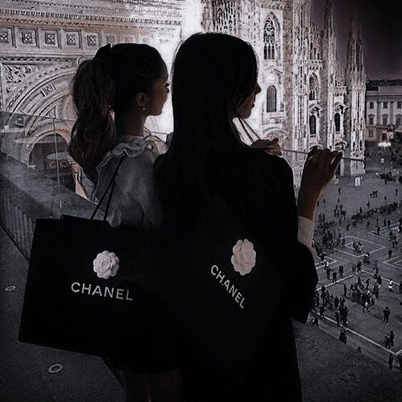 two women standing in front of a building with chanel bags on their backs, looking at the city