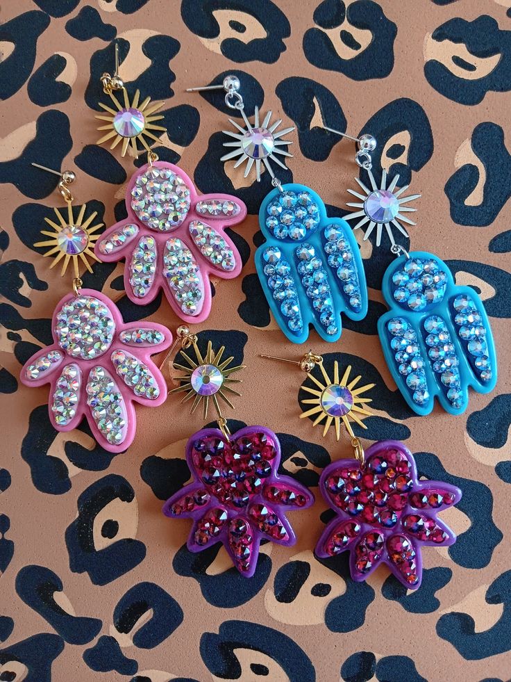 four different colored hair clips on top of a leopard print table with blue, pink and purple flowers