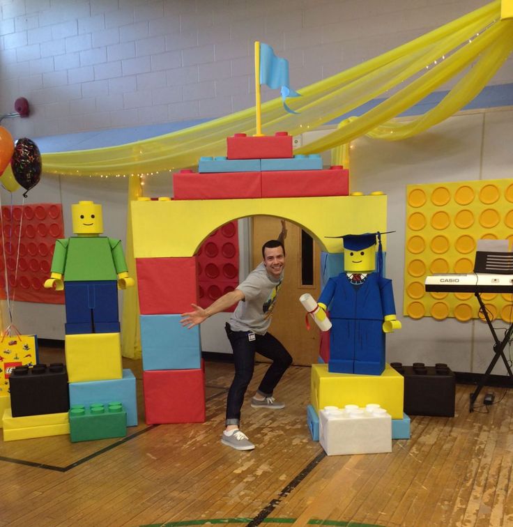 a man standing in front of a building made out of legos on a wooden floor