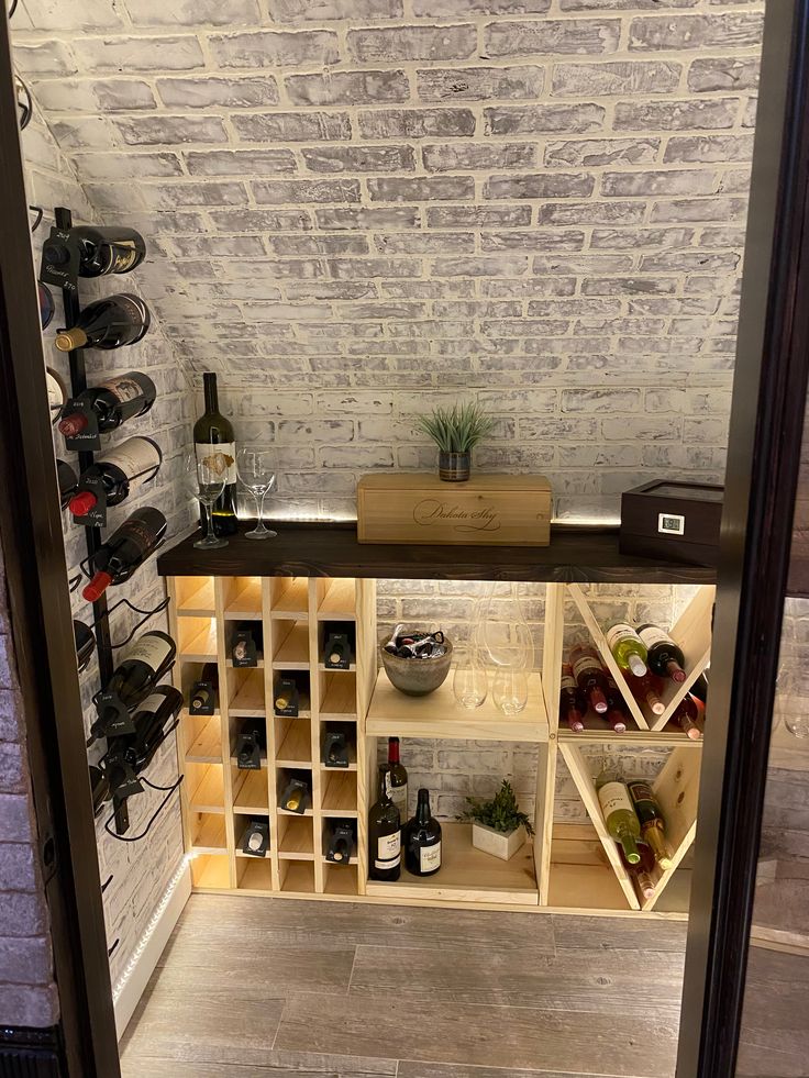 a wine cellar with several bottles and glasses on the shelves in front of brick wall