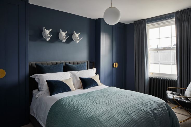 a bedroom with dark blue walls and white bedding, along with two lamps on the wall