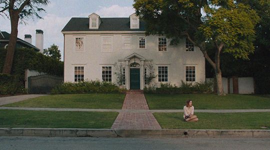 a woman sitting on the grass in front of a white house