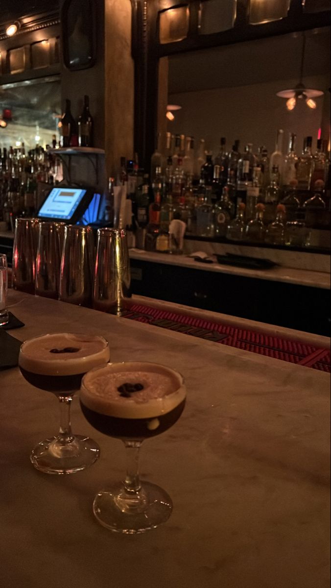 two glasses filled with drinks sitting on top of a bar