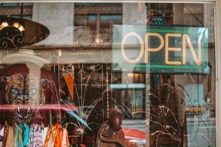 an open sign is in the window of a clothing store that sells handmade masks