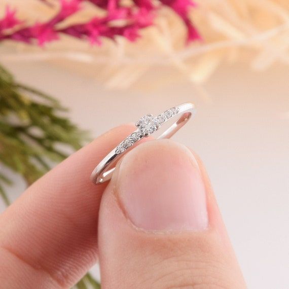 a hand holding a diamond ring with flowers in the background