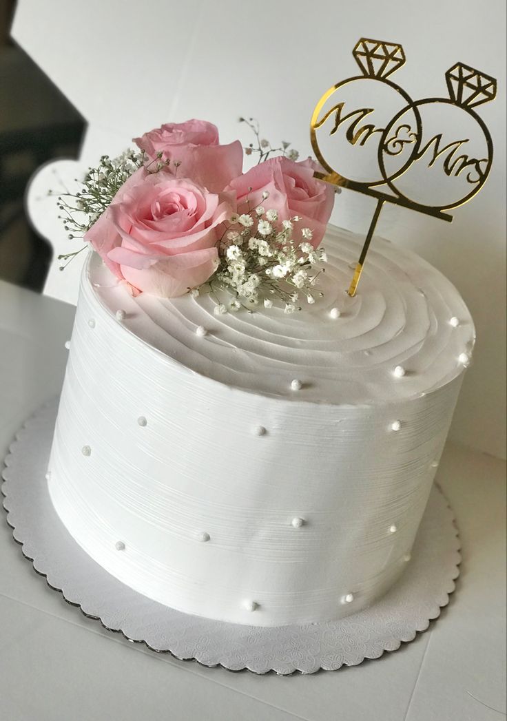 a white cake with pink flowers and a gold monogrammed topper on it