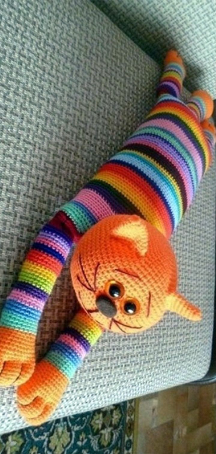 an orange cat is laying on the couch with its legs wrapped in colorful yarns