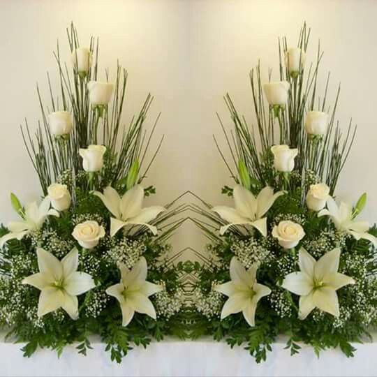 two vases with white flowers and greenery on top of a table in front of a mirror