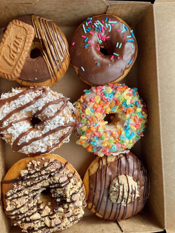 a box filled with lots of different flavored donuts covered in frosting and sprinkles