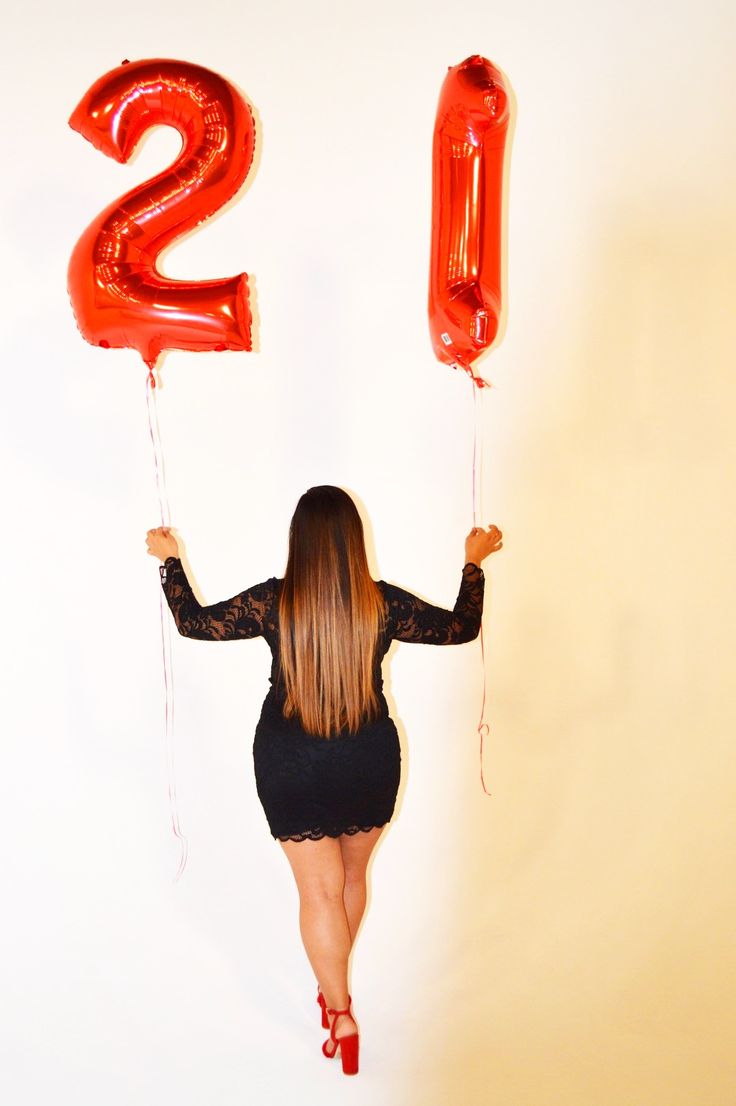 a woman holding two red balloons in the shape of the number twenty and one with her hands