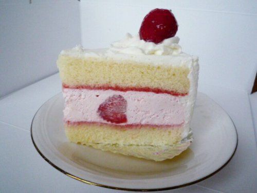 a piece of cake on a white plate with a strawberry on top and whipped cream