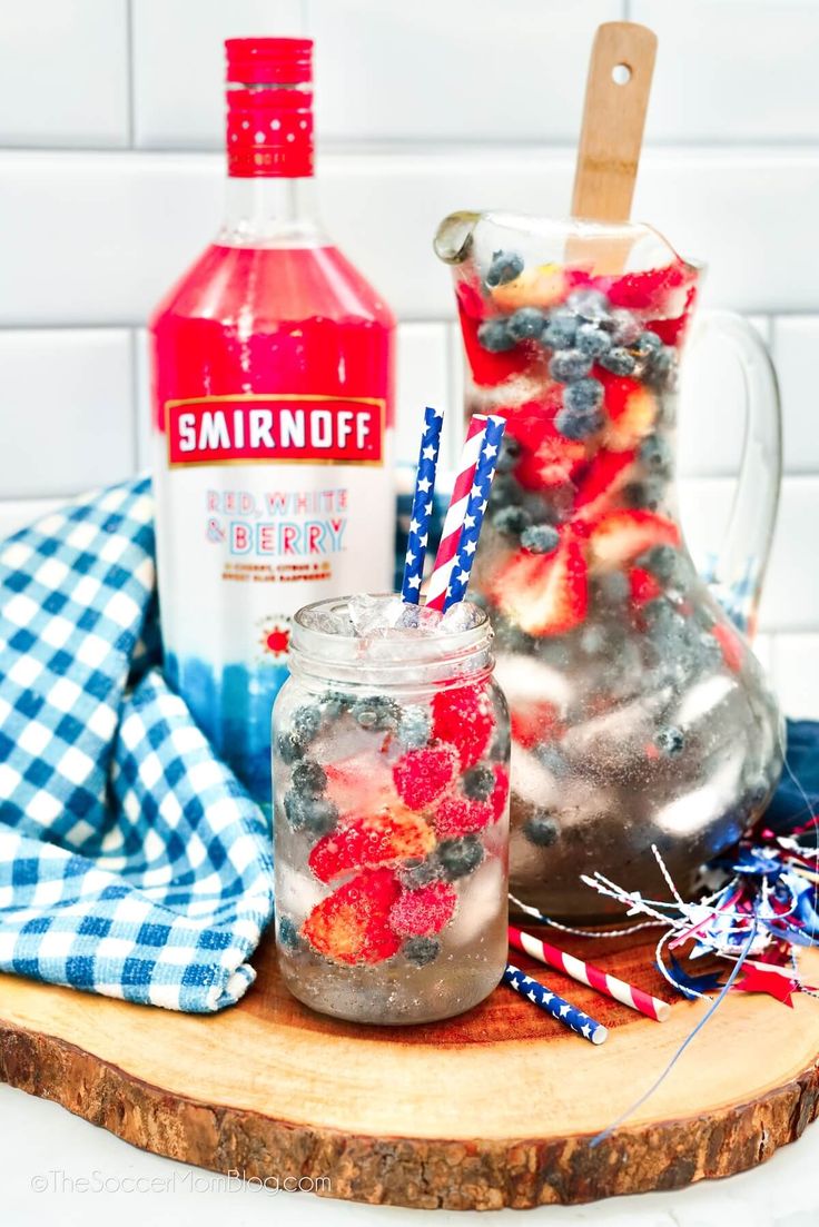 two mason jars filled with berries, ice and strawberries on top of a cutting board