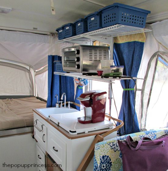 the inside of a camper with blue curtains and white appliances on it's shelves