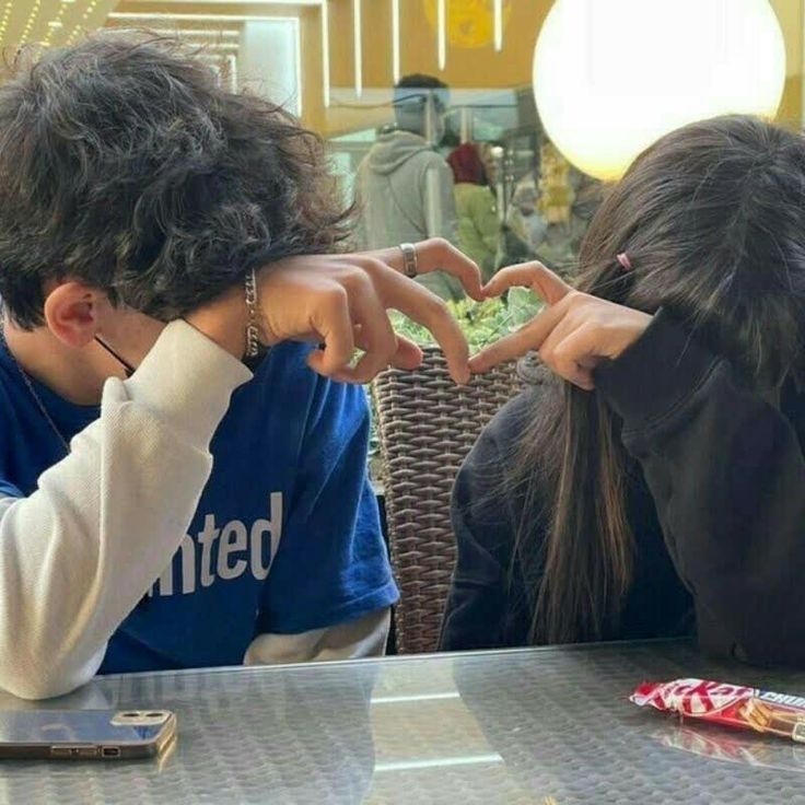 two people sitting at a table with their hands in the shape of a heart,