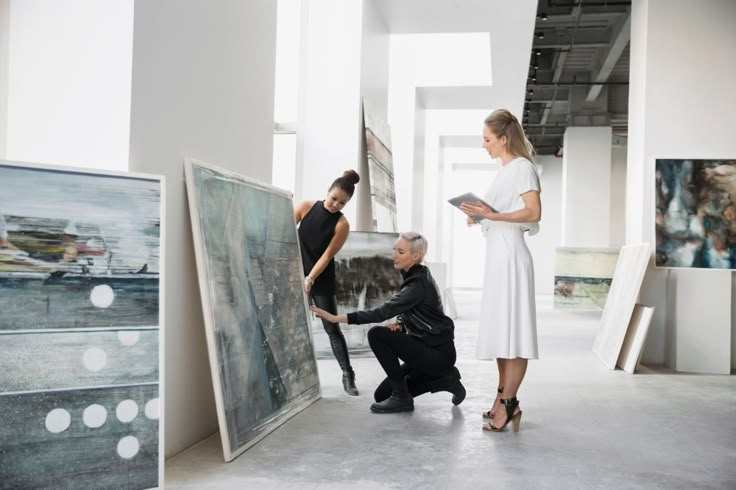 two people are looking at paintings in an art gallery while another person is kneeling down