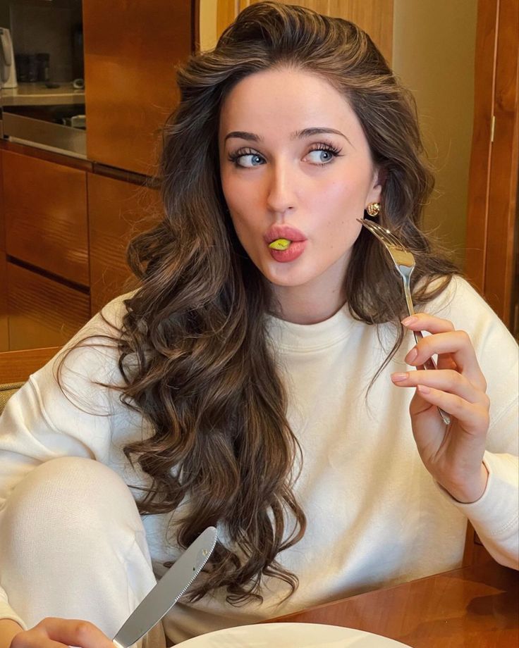 a woman sitting at a table with a fork and knife in her mouth