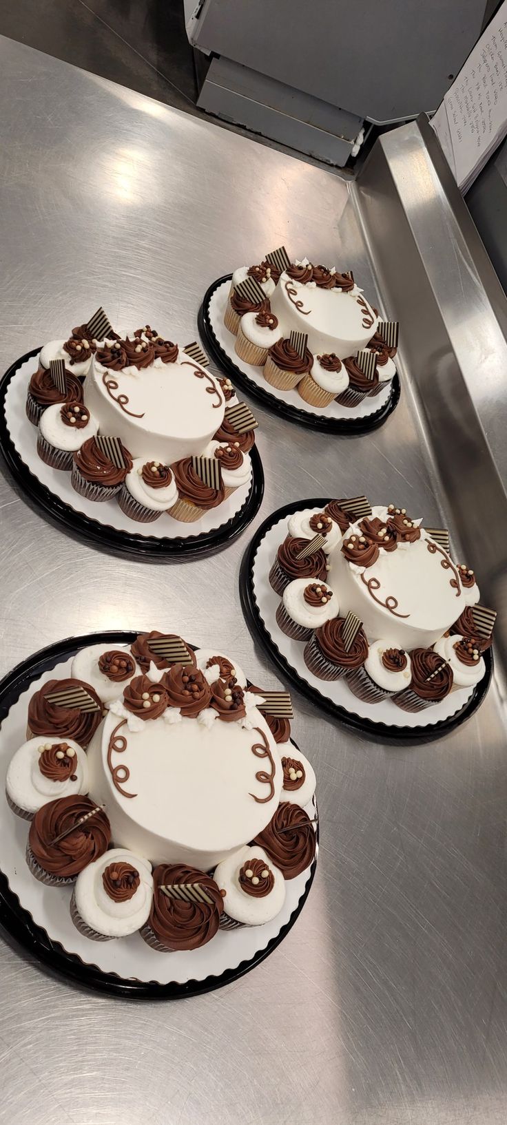 three cakes sitting on top of a metal counter covered in frosting and chocolate decorations