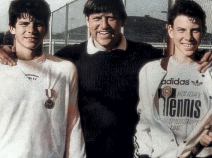 three men standing next to each other in front of a fence with their arms around one another