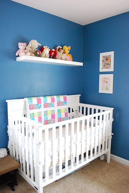 a white crib in a blue room with stuffed animals on the shelf above it