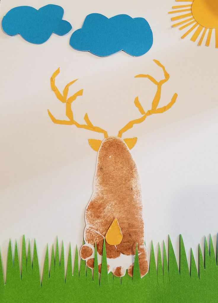 a paper cut out of a deer standing in the grass with clouds and sun above it